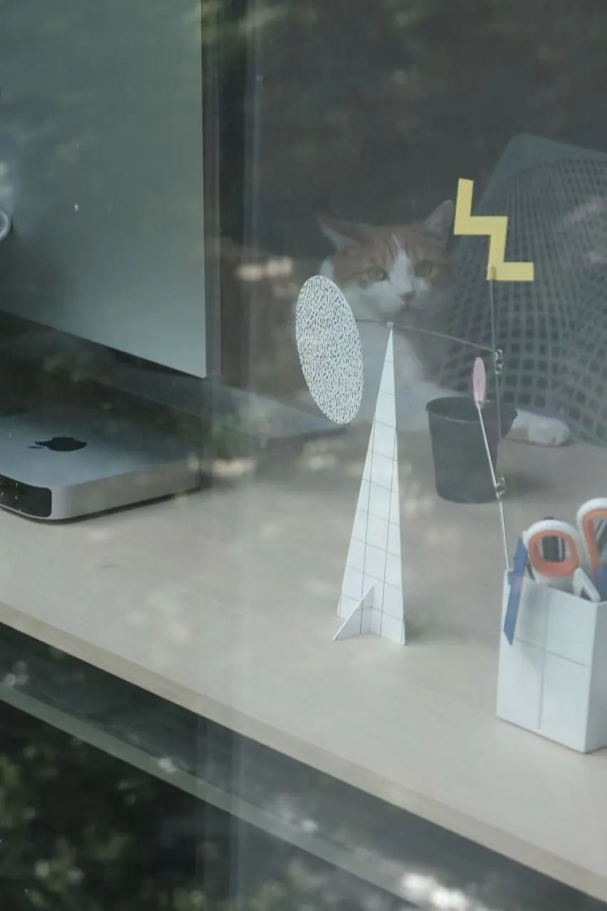 A modern window display featuring a paper decoration with a cat sitting behind it.