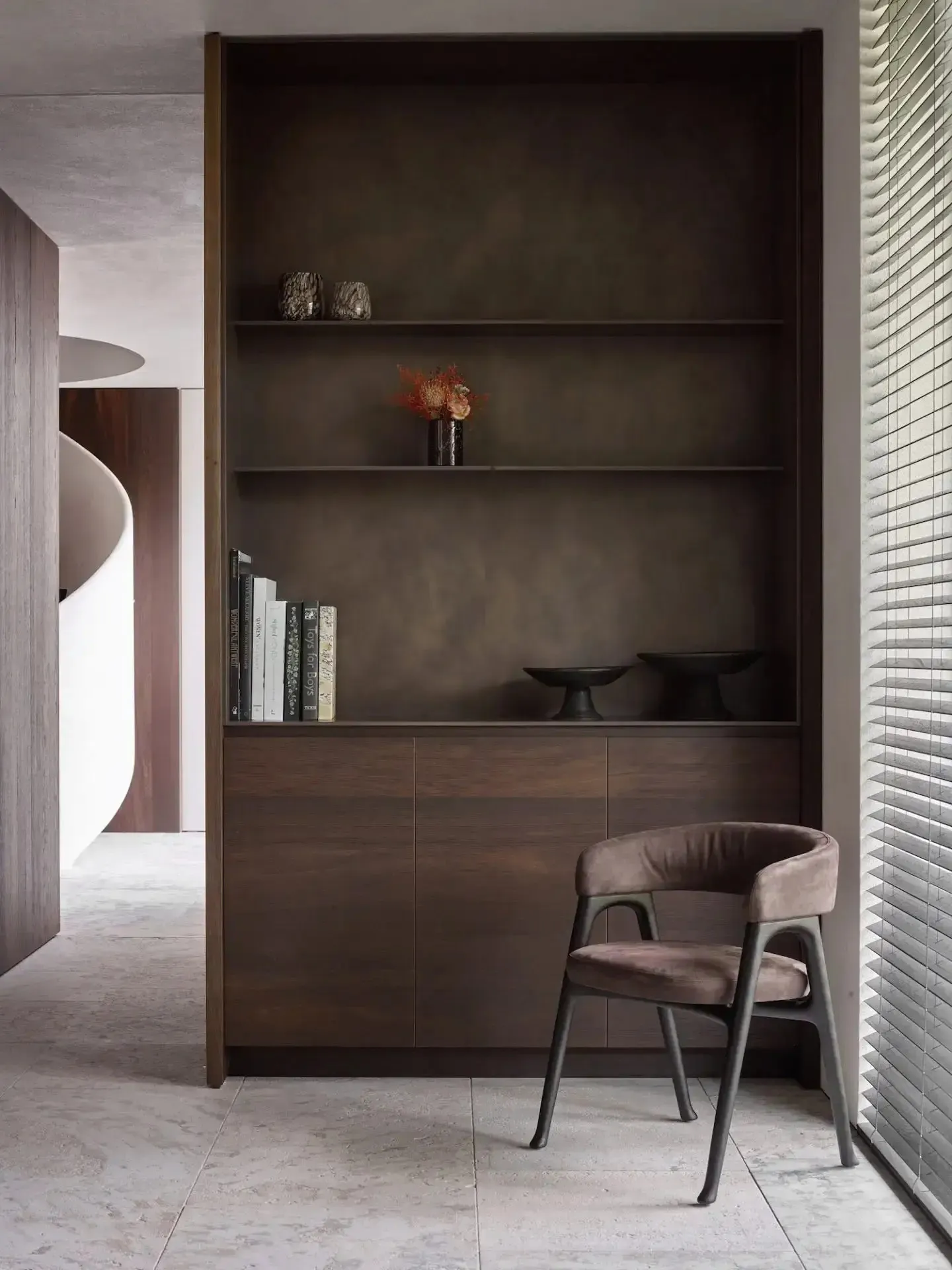 A modern bookshelf with a chair in front of it, featuring a minimalist design with dark wood materials.