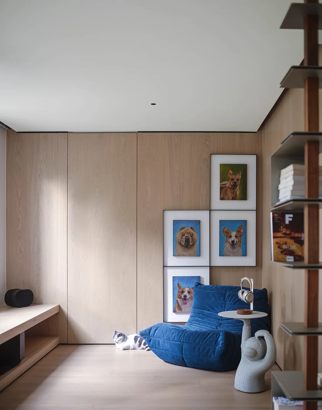 A modern living room with wooden walls, a blue lounge chair, and framed portraits of dogs.