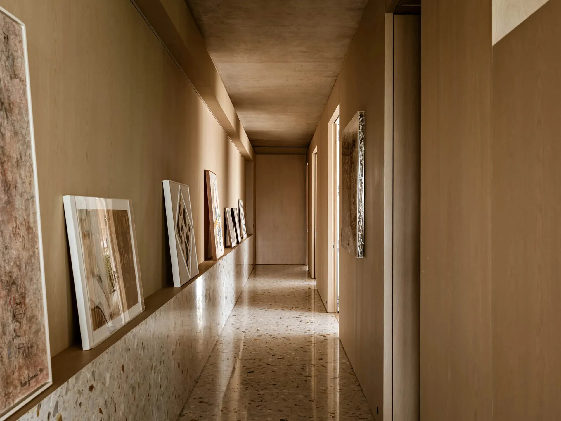 A minimalist corridor with a concrete wall and terrazzo floor, showcasing abstract art hanging along the walls.