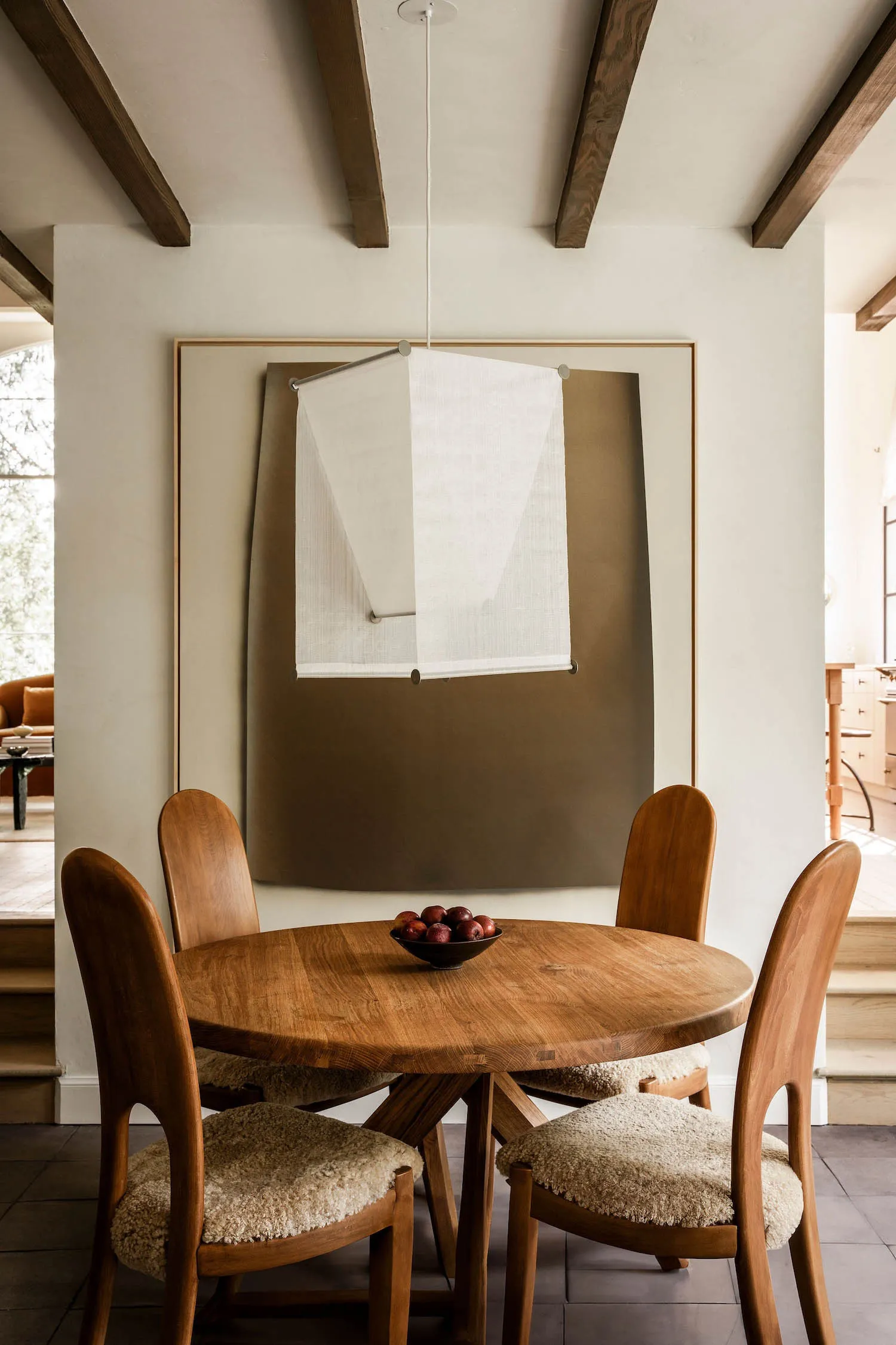 Industrial-style dining room with a circular wooden table, four cushioned wooden chairs, and a wall-mounted light fixture.