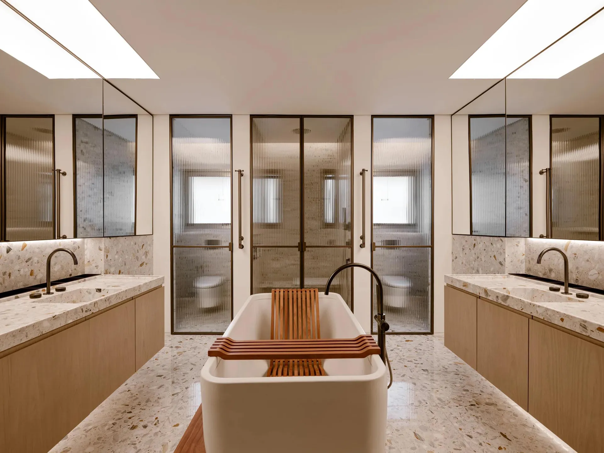A minimalist bathroom featuring a freestanding tub, terrazzo flooring, and sleek white cabinetry.