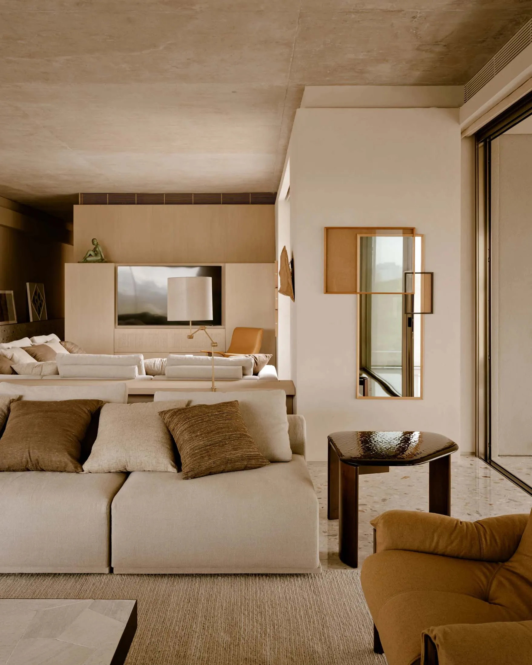 A minimalist living room featuring concrete walls and furniture with earthy tones and textures.