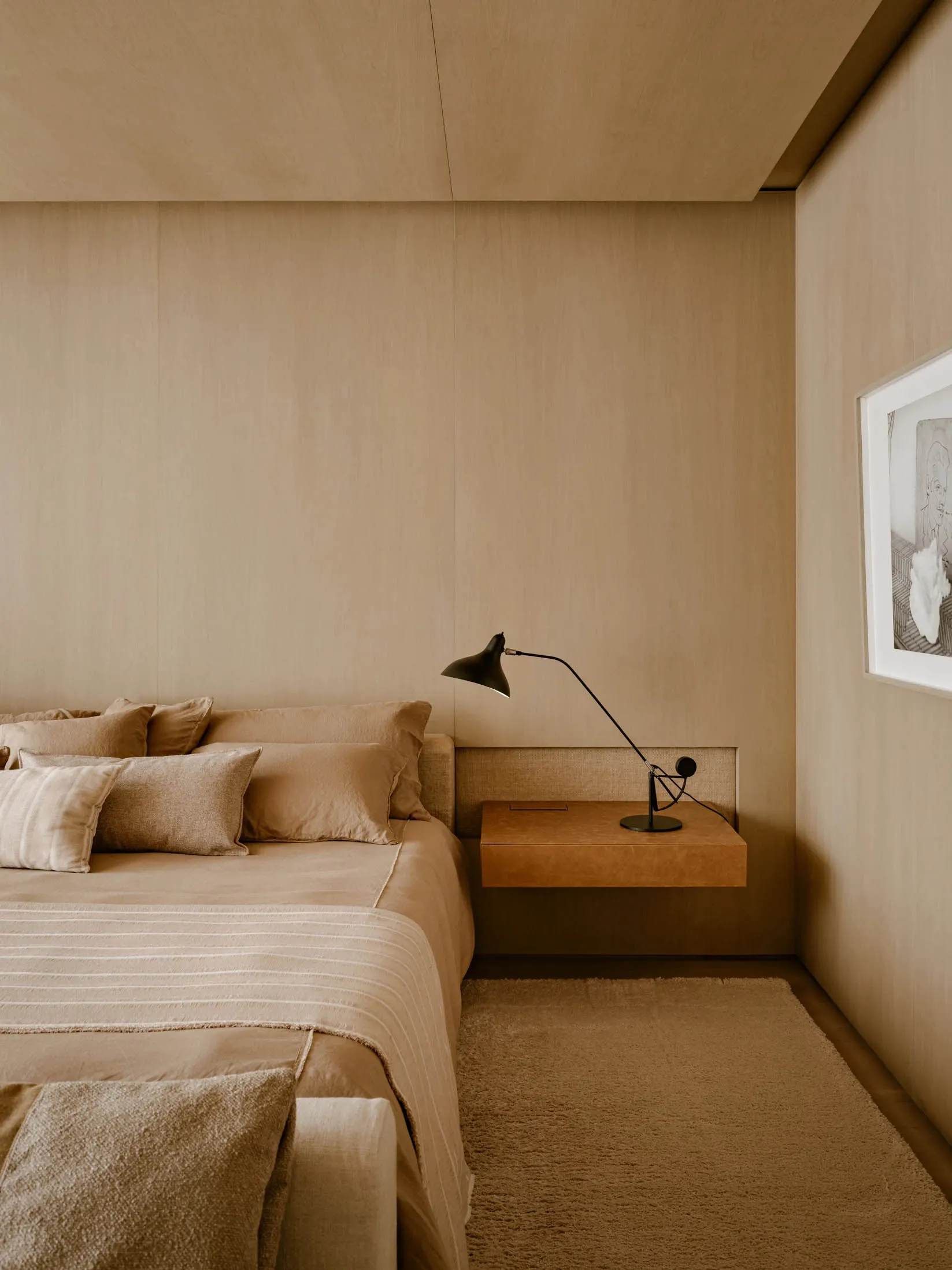 A minimalist bedroom featuring textured wall paneling, a bed with soft linens, and a sleek, floating nightstand with a modern