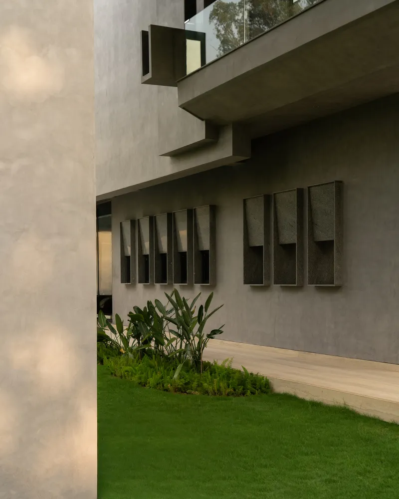 Modern building exterior with concrete and glass materials, featuring green plants and a small garden bed.