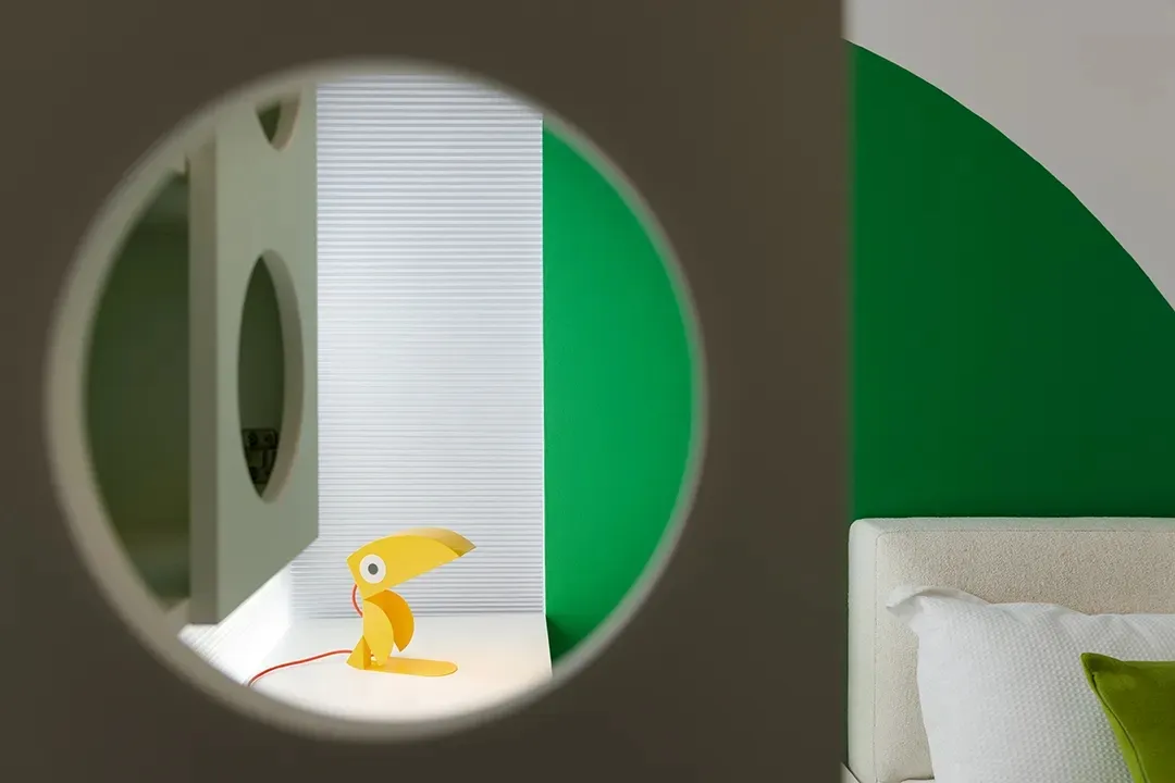 A modern bedroom with a green accent wall and a toucan-shaped lamp on the windowsill.