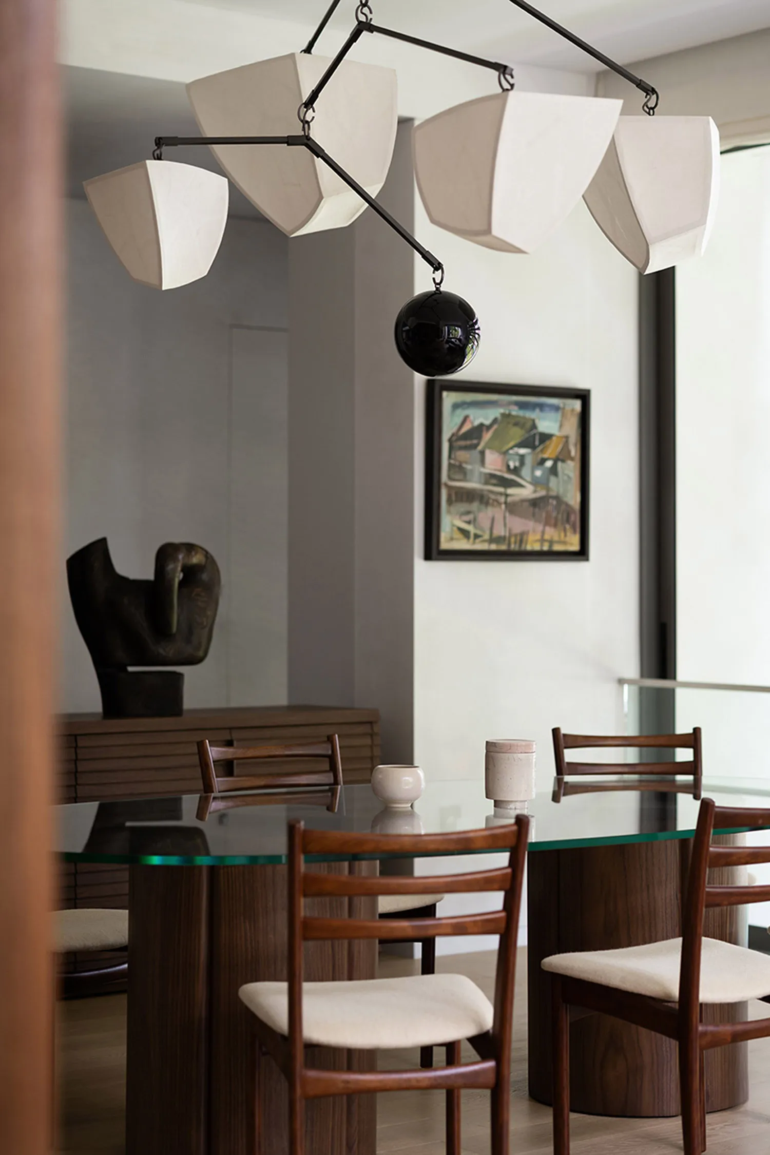 Modern dining room featuring a glass-top dining table with wooden legs and base, paired with upholstered chairs with minimali