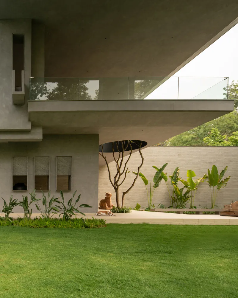 A modern industrial residential exterior featuring concrete, glass, and lush green plants.
