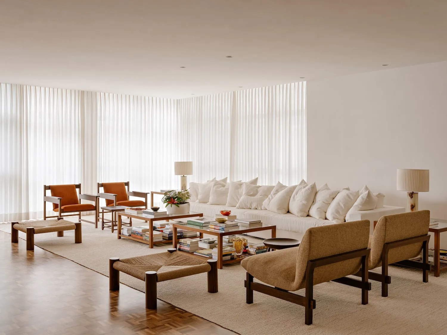 Modern minimalist living room featuring white walls, neutral-toned furniture, and a large window with sheer curtains.