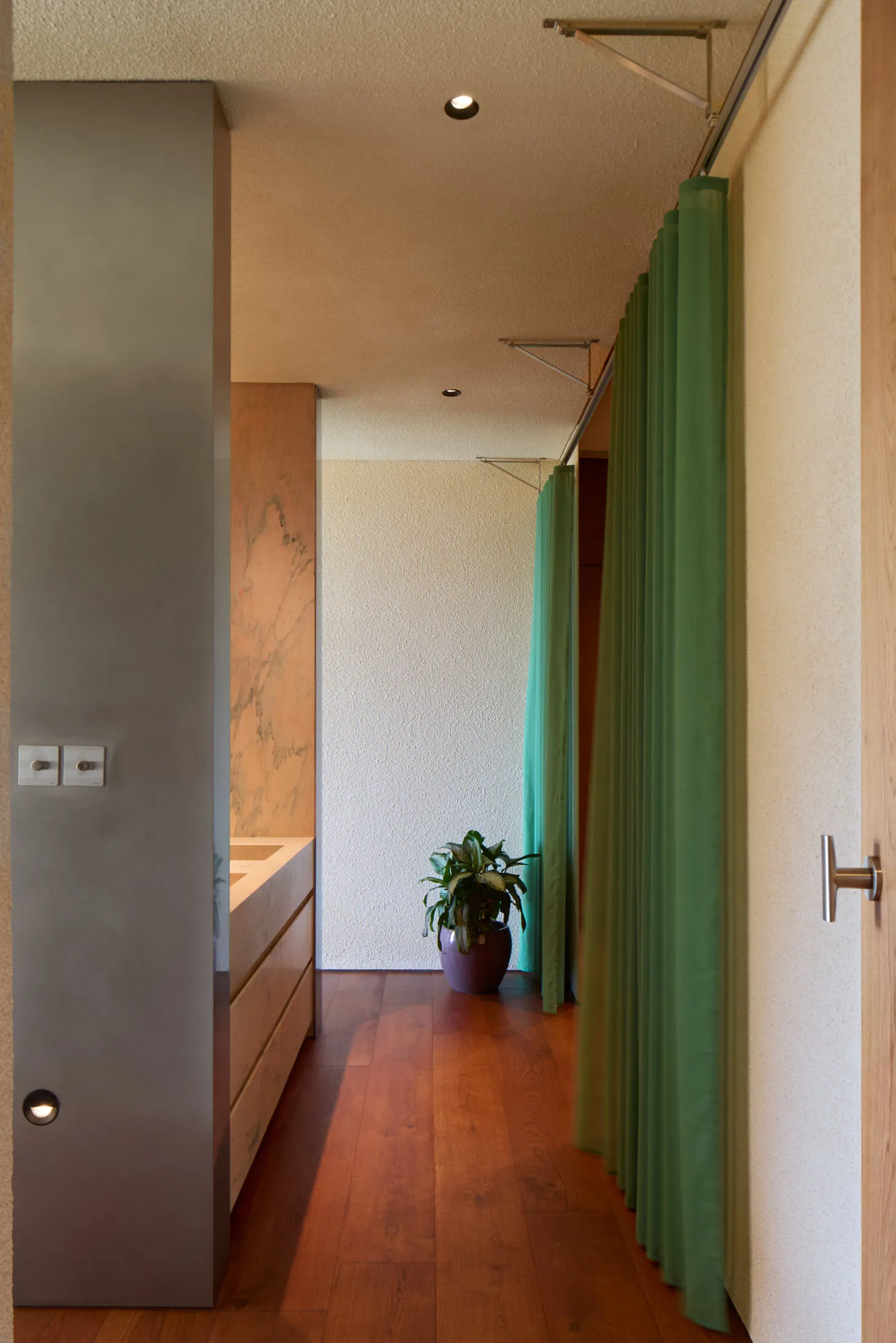 A minimalist apartment entryway featuring green curtains on a wooden floor.