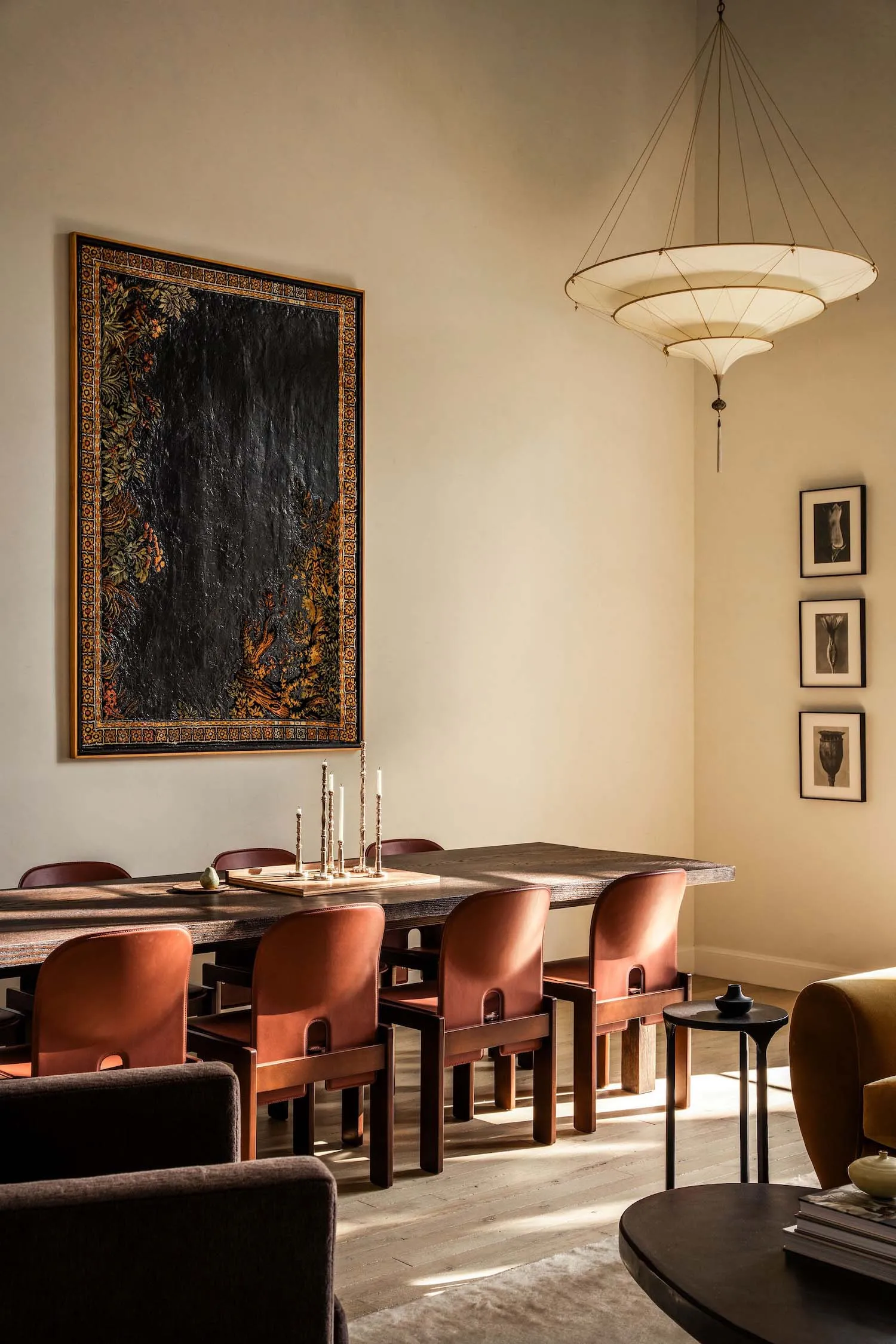 A modern dining room with wooden furniture, leather chairs, metal accents, and a large artwork on the wall.