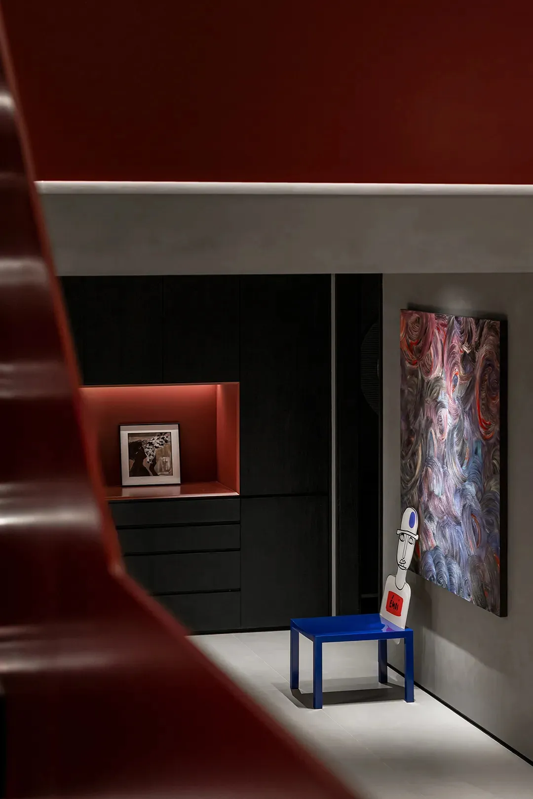 A modern living room with dark furniture, red accent wall, and abstract art.