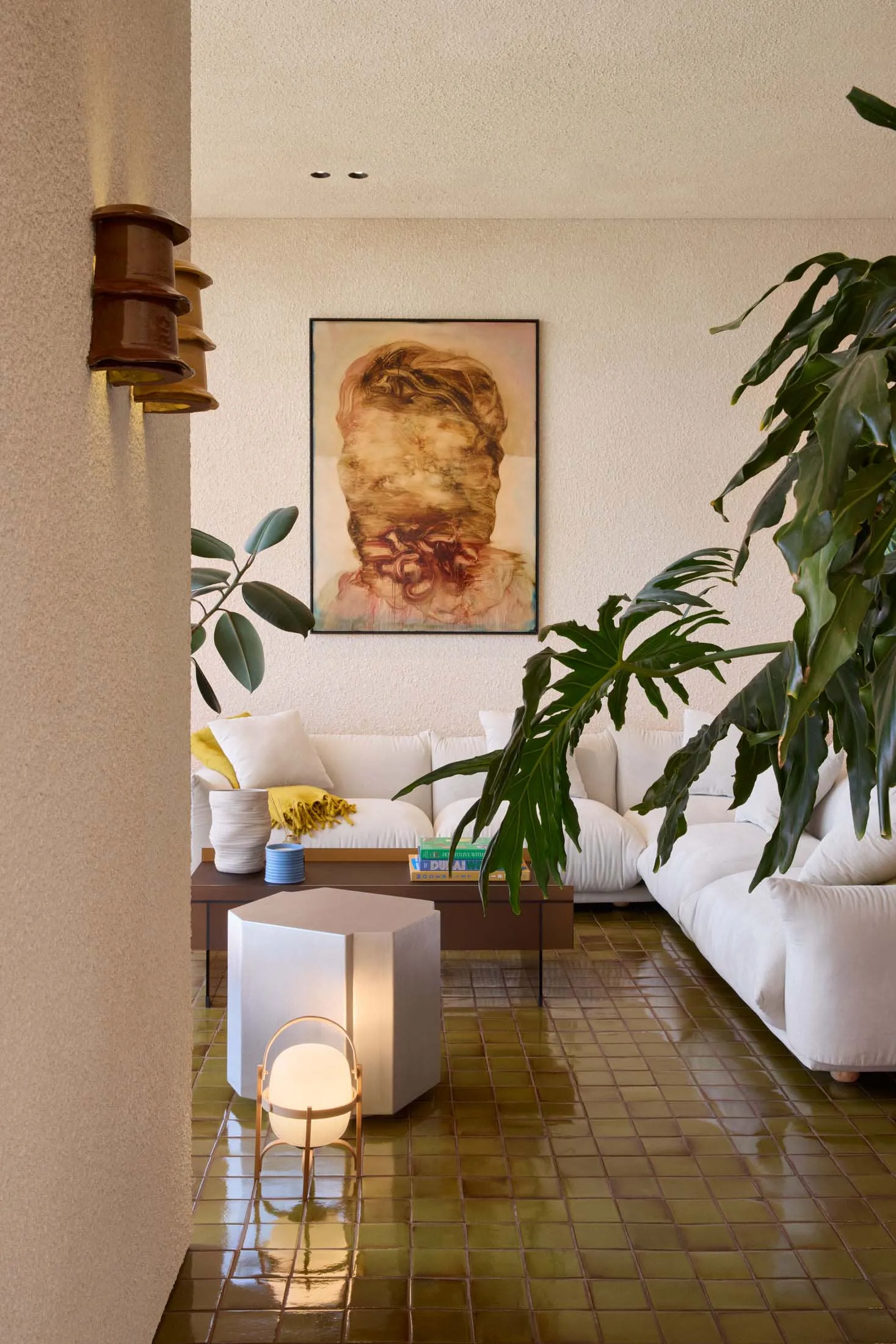 A modern, minimalist living room with concrete floors, white sofas, and large green plants.