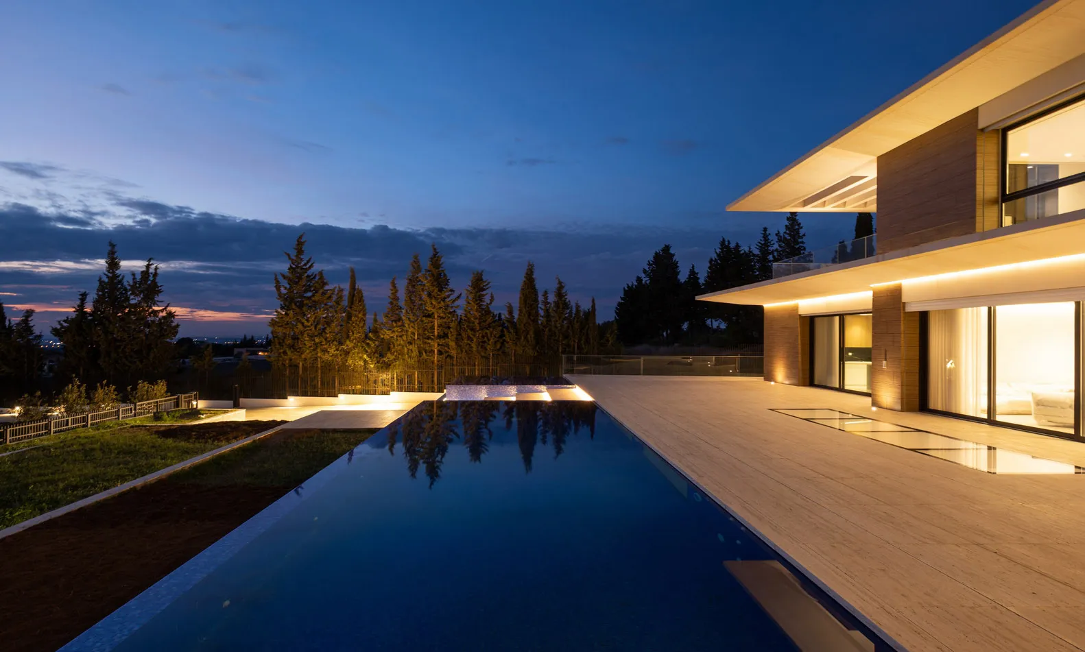 An exterior view of a modern villa during dusk, featuring wooden exterior, a reflective swimming pool, and a serene outdoor s
