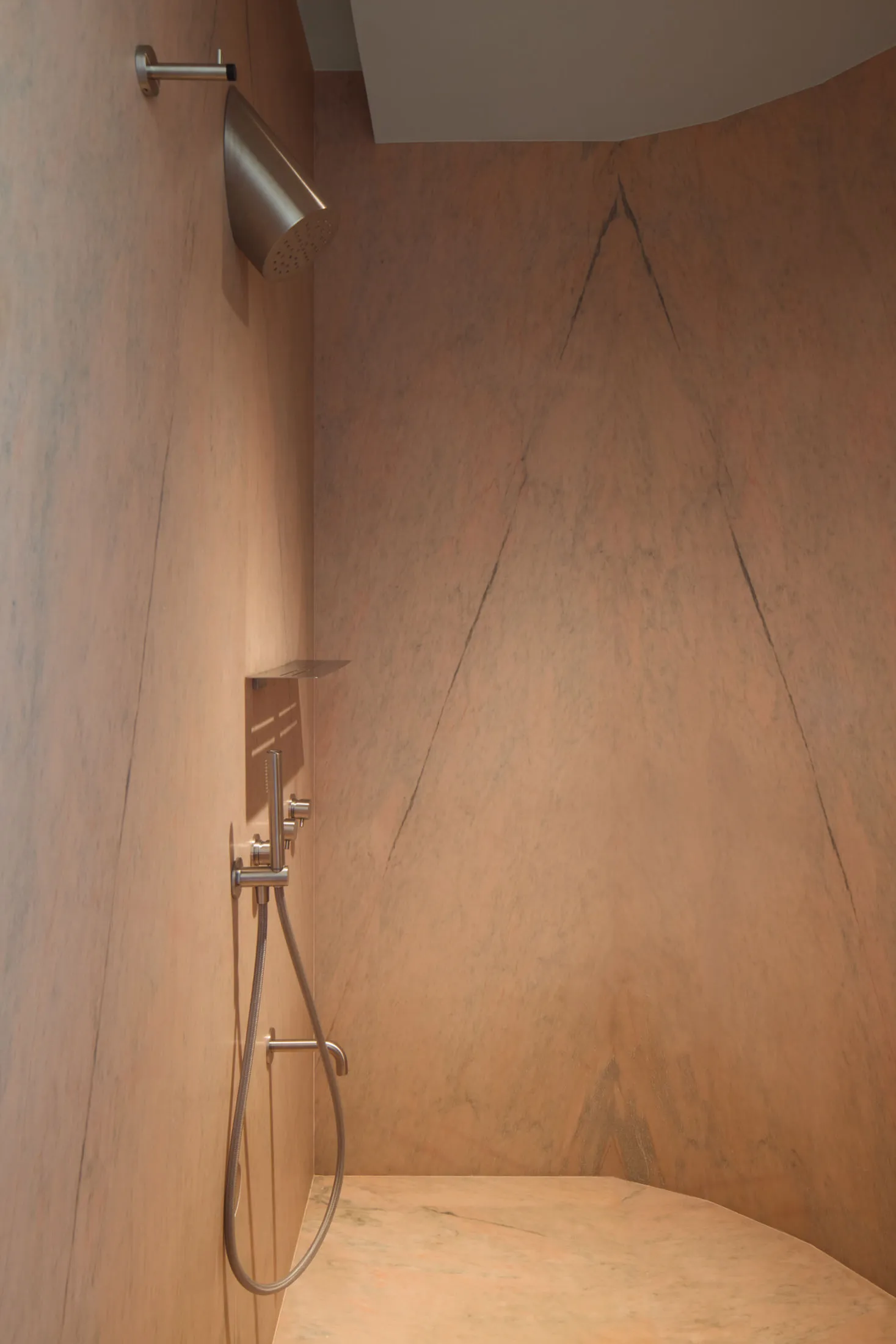 A minimalist bathroom with a sandstone wall and floor, featuring a modern shower head and fixtures.