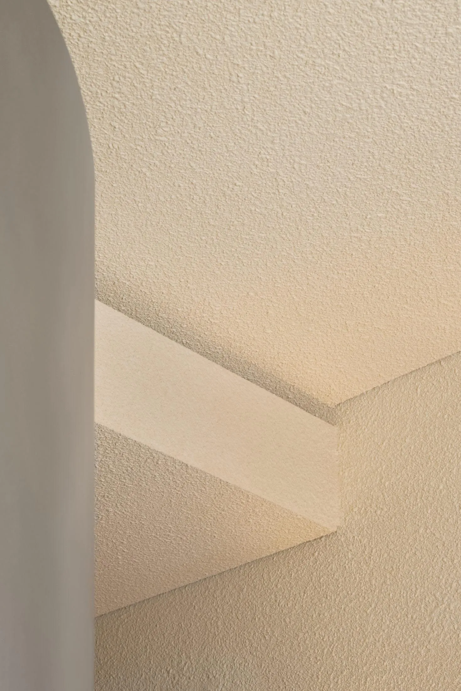 Low-angle photograph of a minimalist staircase with textured beige walls and steps.