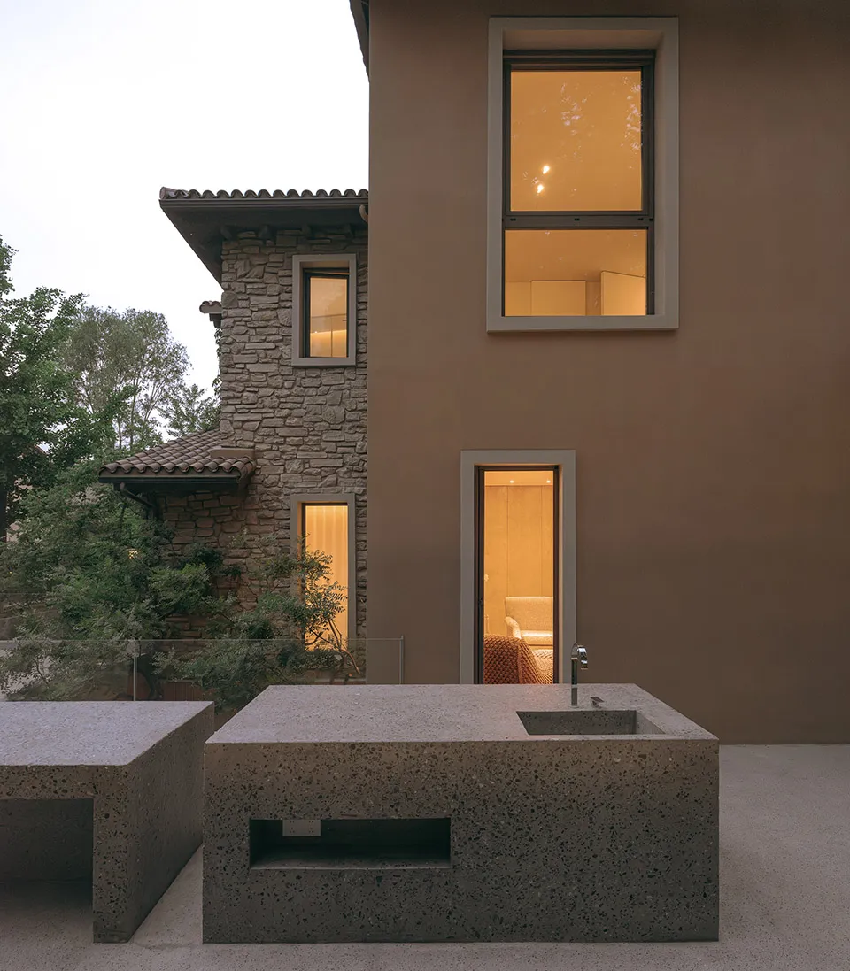 Modern house with concrete exterior, showing evening lighting through windows and a contemporary outdoor kitchen island.