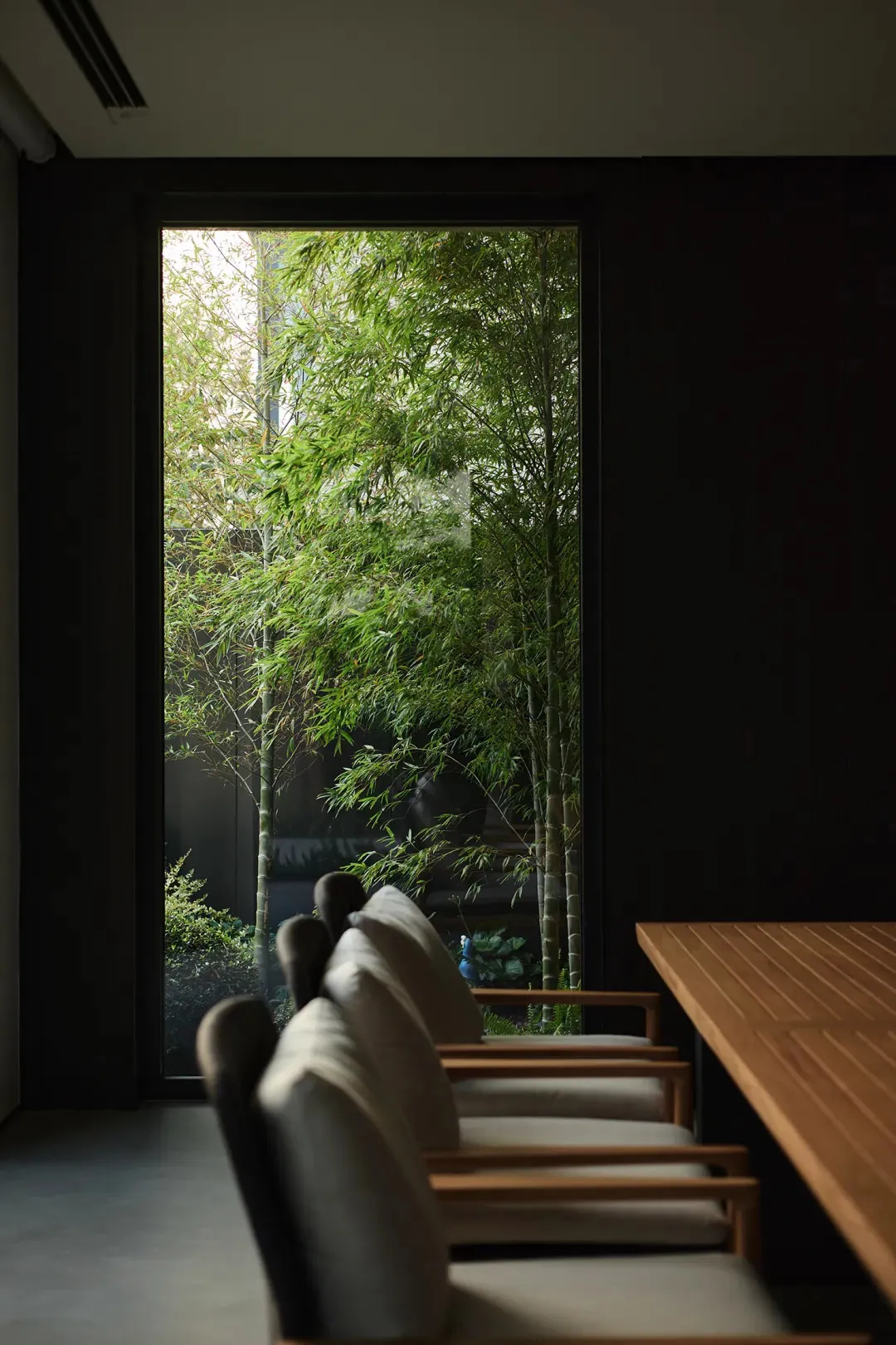 A modern living room with wooden furniture and a view of greenery outside through a large window.