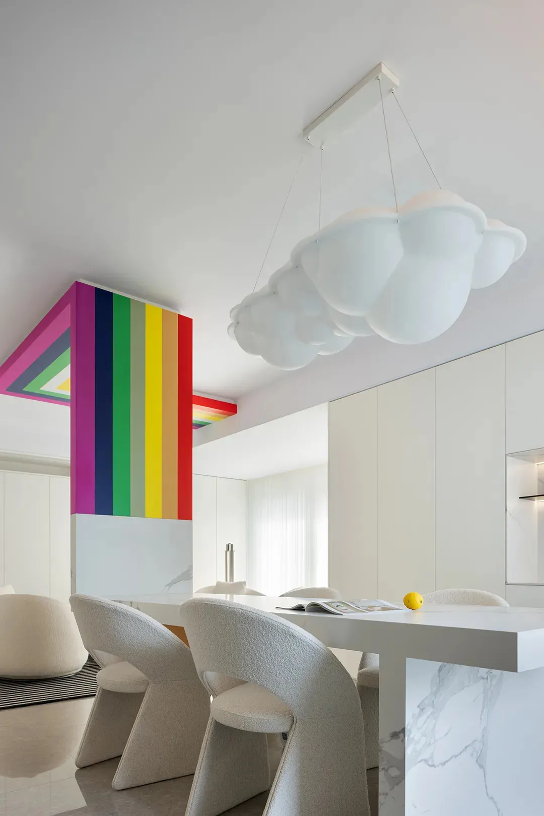 A modern kitchen with a white marble countertop, white chairs, and a colorful wall art.