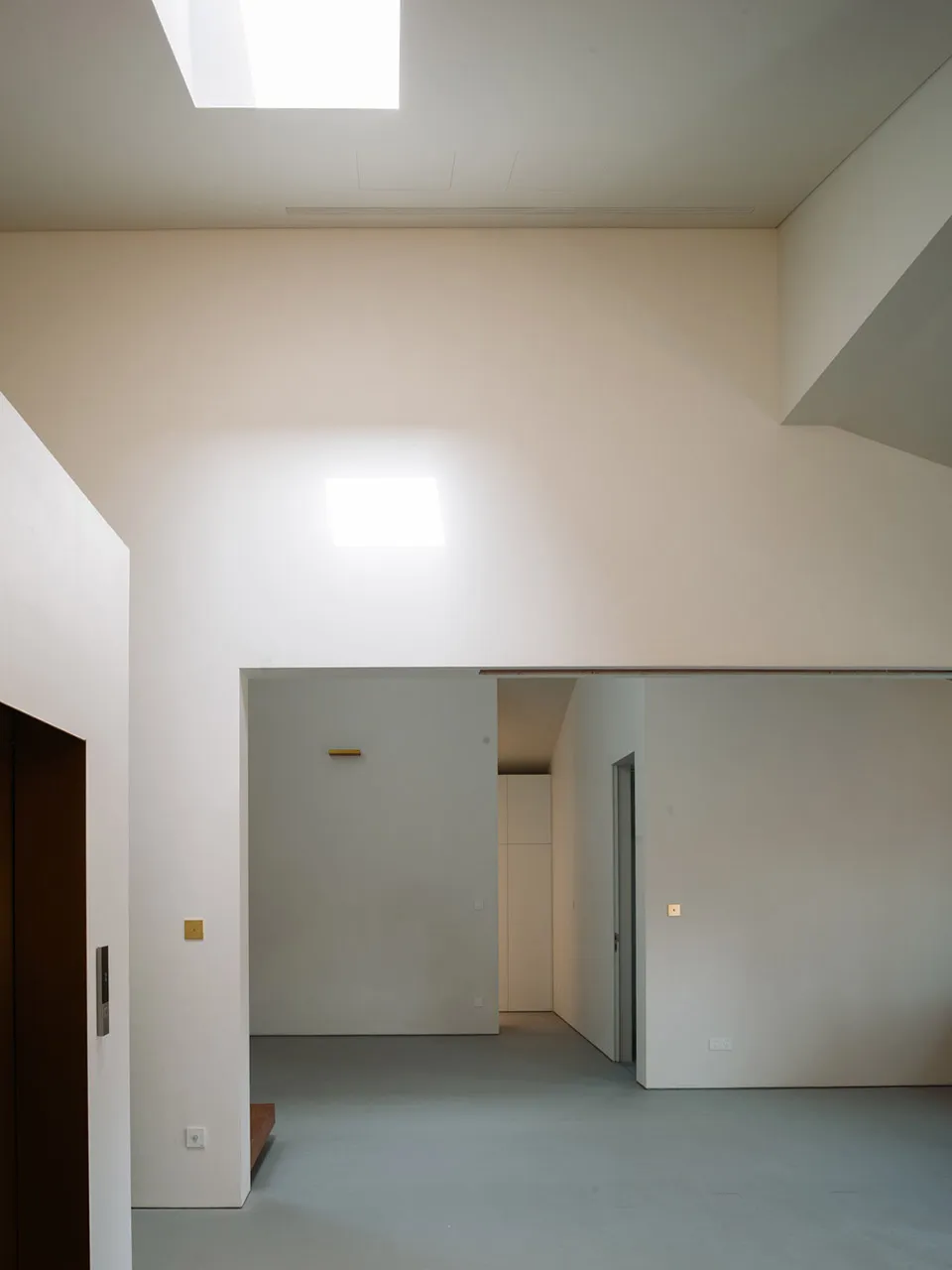 A modern minimalist living room with exposed concrete walls and ceiling, featuring a door with a black frame, two skylights,