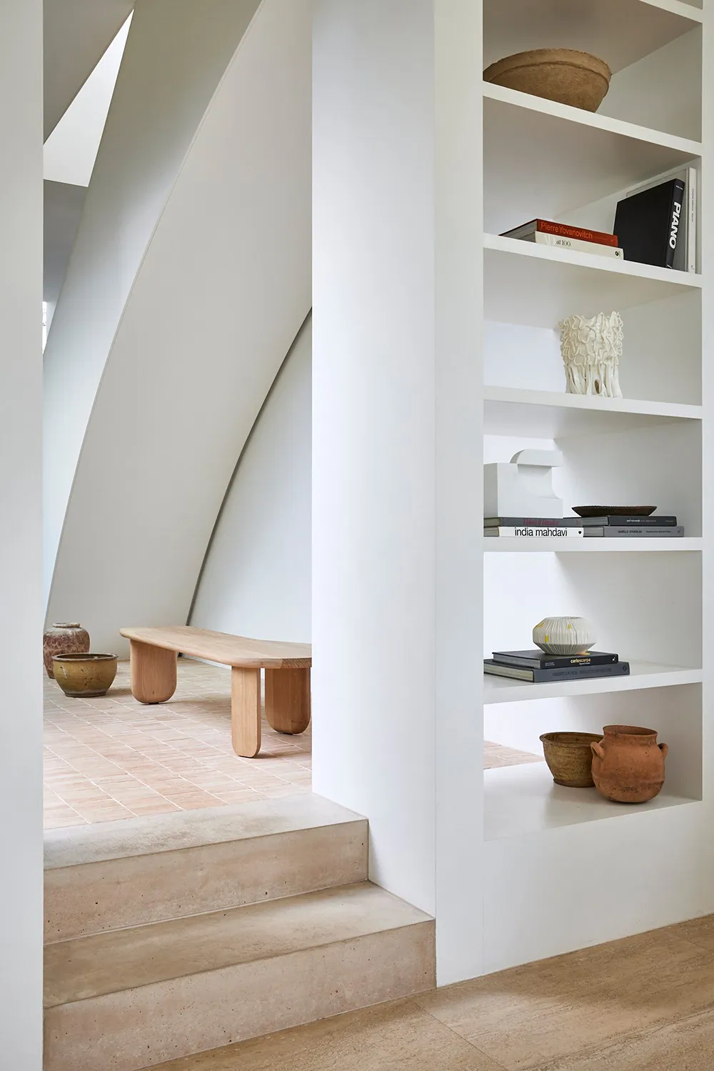 Modern staircase made of wood and concrete with minimalist design aesthetics, featuring a built-in shelf with books, vases, a