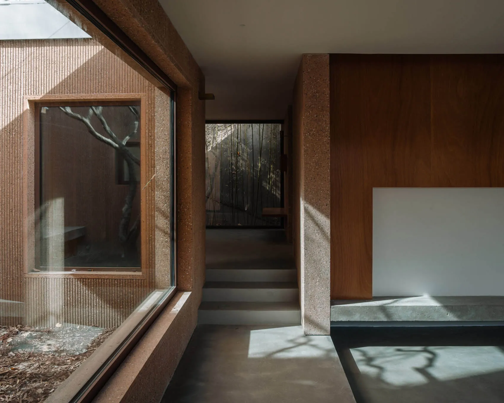 An interior space with minimalist design, featuring concrete walls, large windows, and natural light.