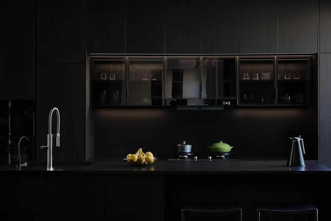 Modern kitchen with black countertops and cabinets, featuring stainless steel appliances and a bowl of lemons.