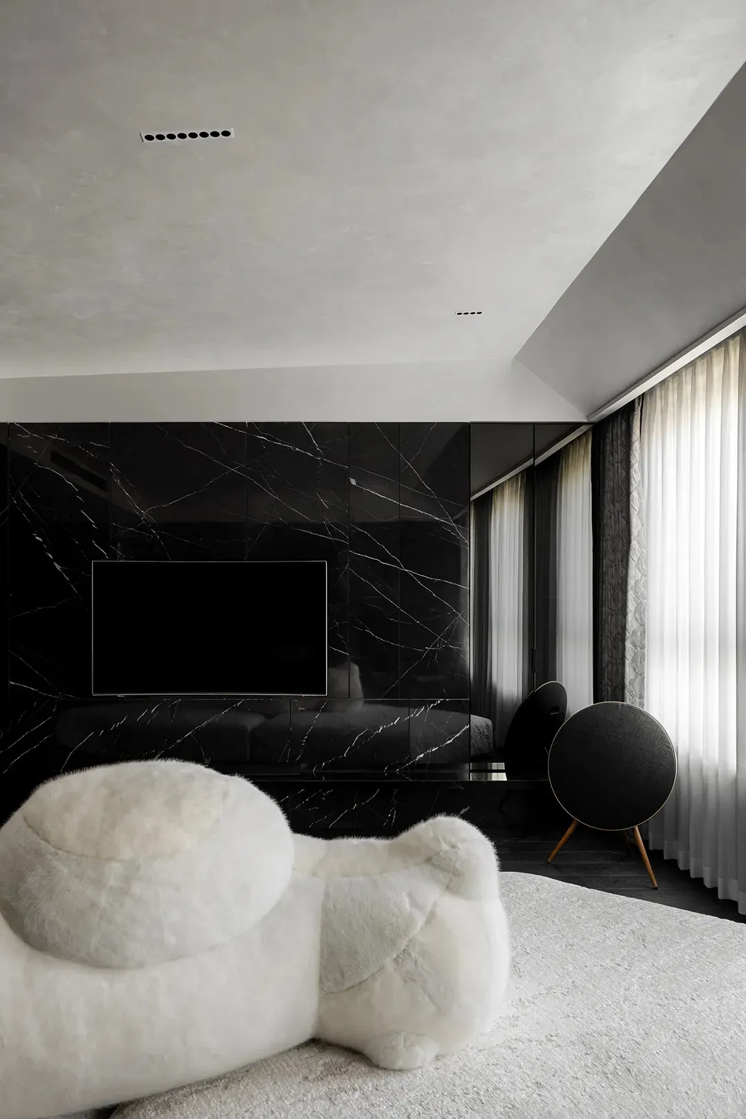 A modern bedroom with black marble walls, white furniture, and a large window.