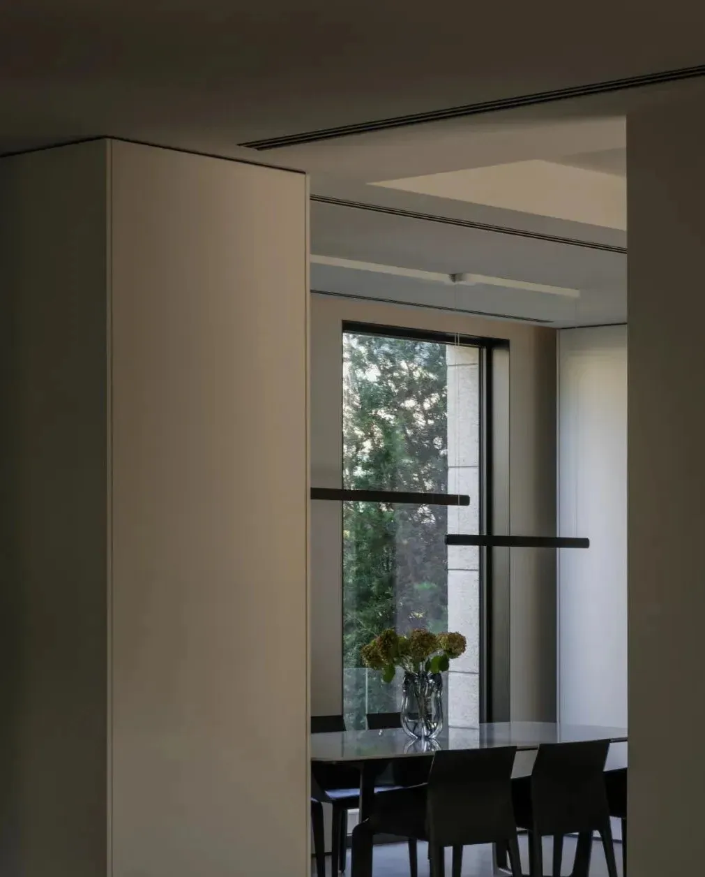 Modern dining room featuring a glass window, black chairs, and a round glass table with a vase of flowers.