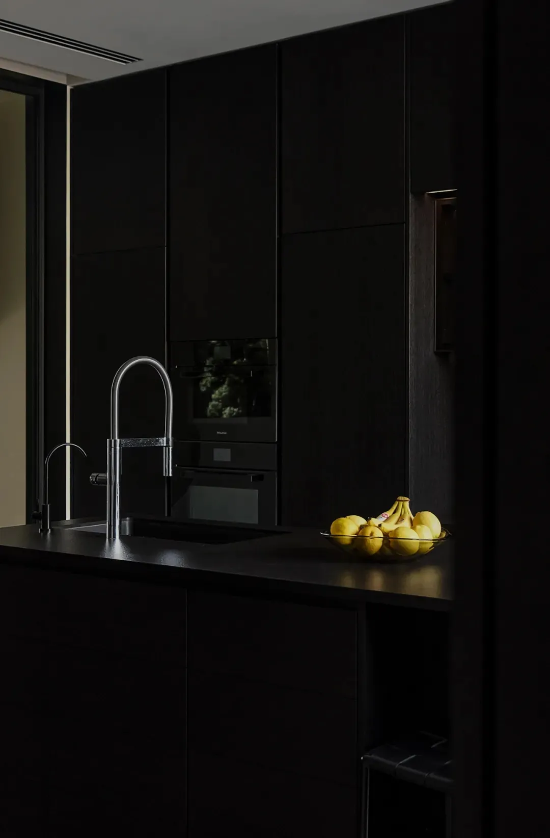 A modern minimalist kitchen with black cabinets, stainless steel appliances, and a black countertop with metallic accents.