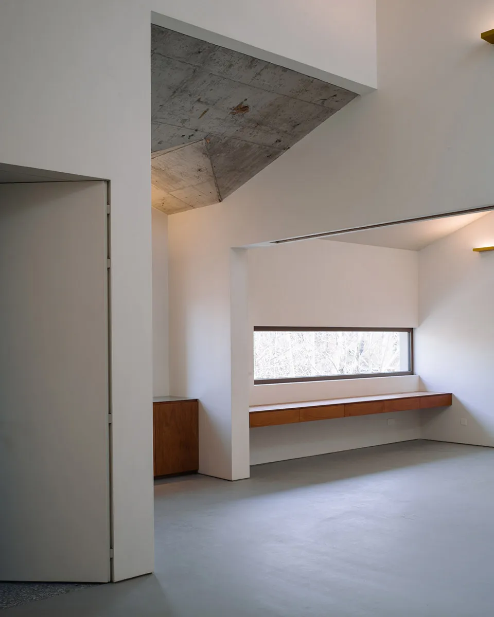 Modern minimalist living room with concrete walls, wood furniture, and large window.