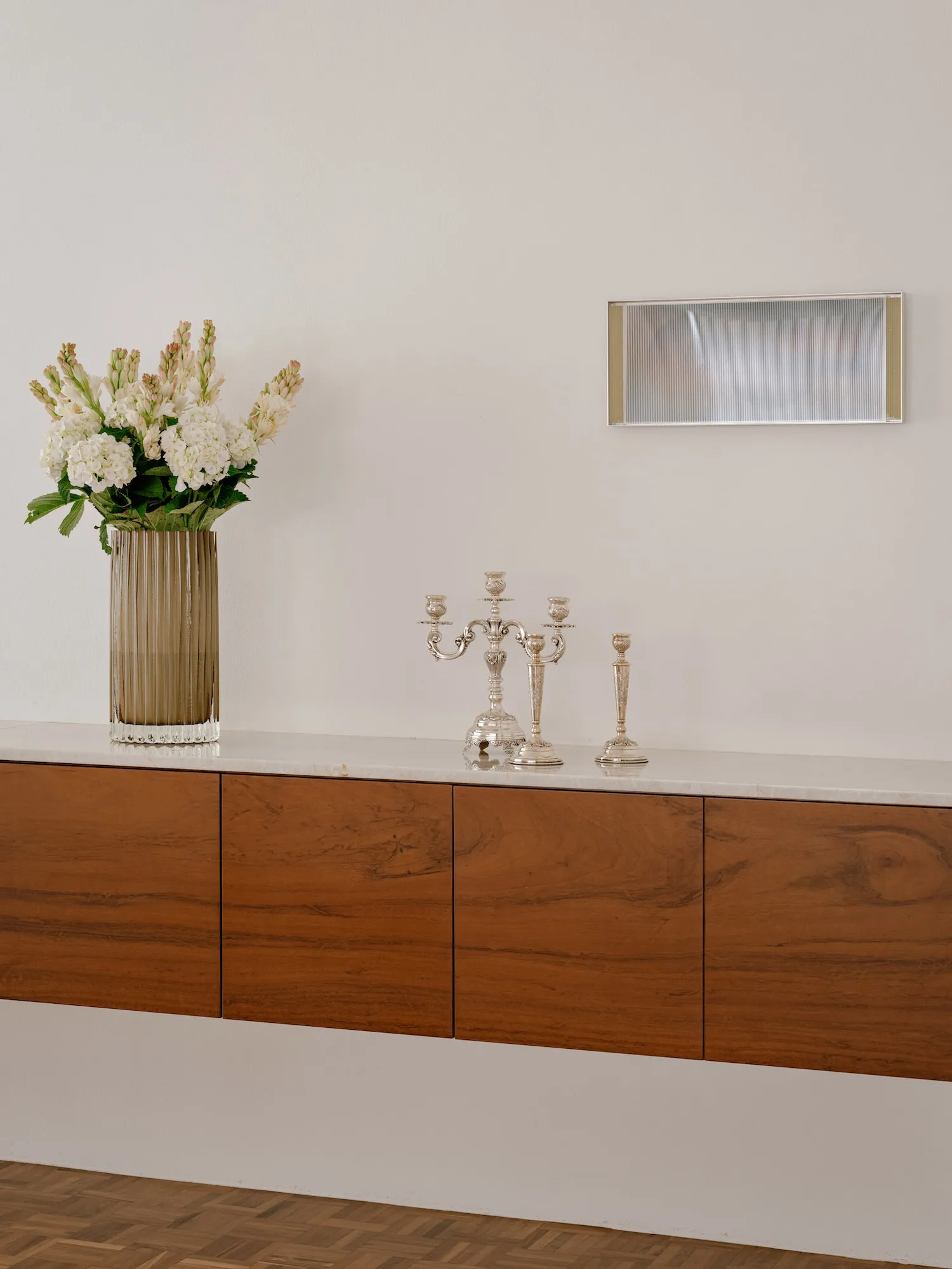 A modern cabinet made of wood with a marble top, featuring decorative elements like a vase of flowers and silver candlesticks