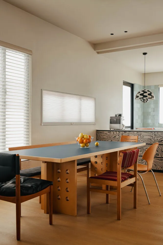 A modern dining room featuring a wooden table with a blue surface, surrounded by chairs of various designs.