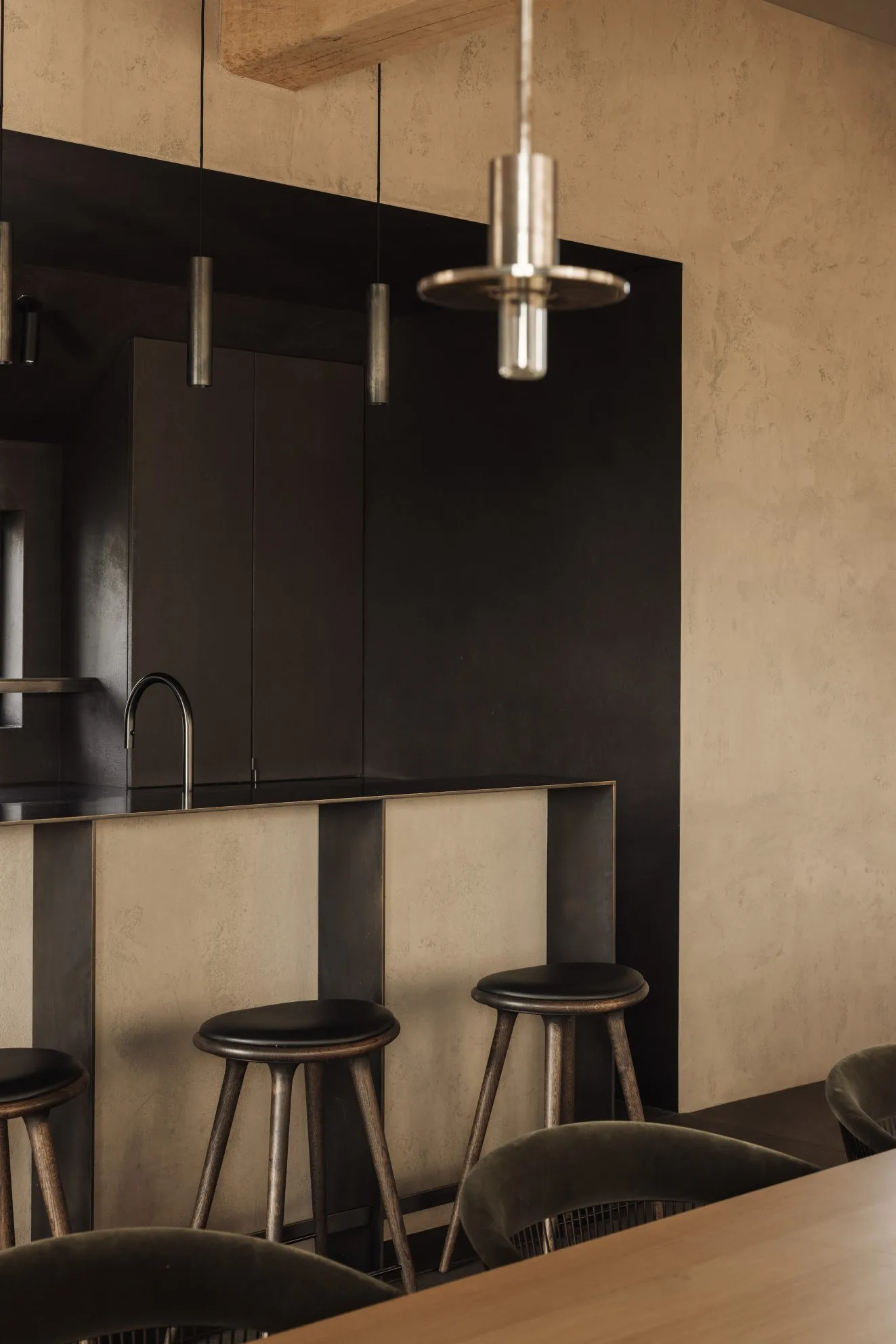 Modern industrial kitchen featuring a sleek black counter, wooden stools, and metal light fixtures.