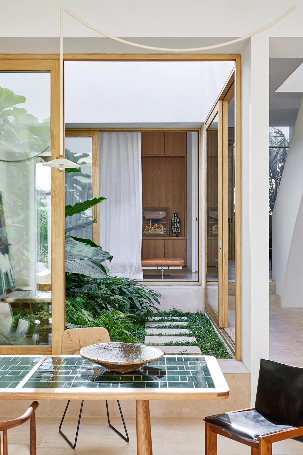 A modern living space with wooden floors and a tile floor, featuring a glass wall, indoor plants, and a cozy seating area.