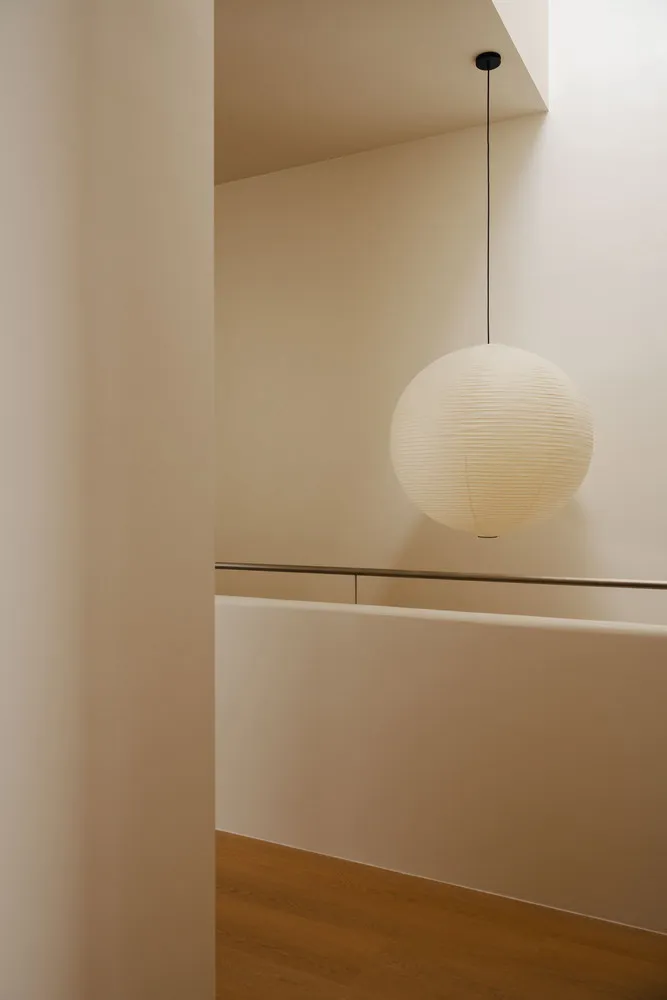 A black-wire paper lamp hangs from the ceiling in a modern stairwell.