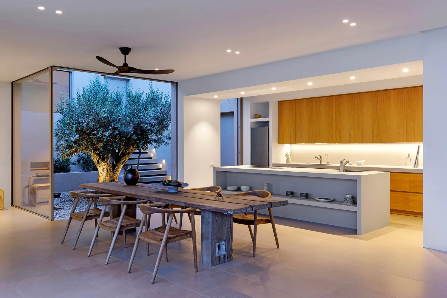 A modern kitchen with a wooden table and chairs, featuring a large tree in the background.