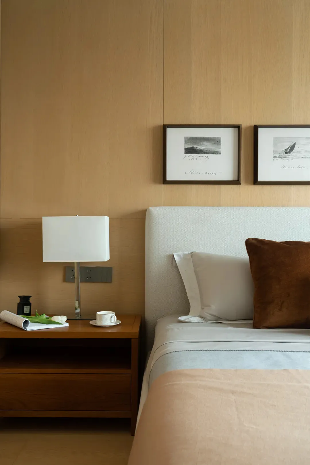A contemporary bedroom featuring a white upholstered bed with a wooden bedside table, light-colored walls, and framed art on