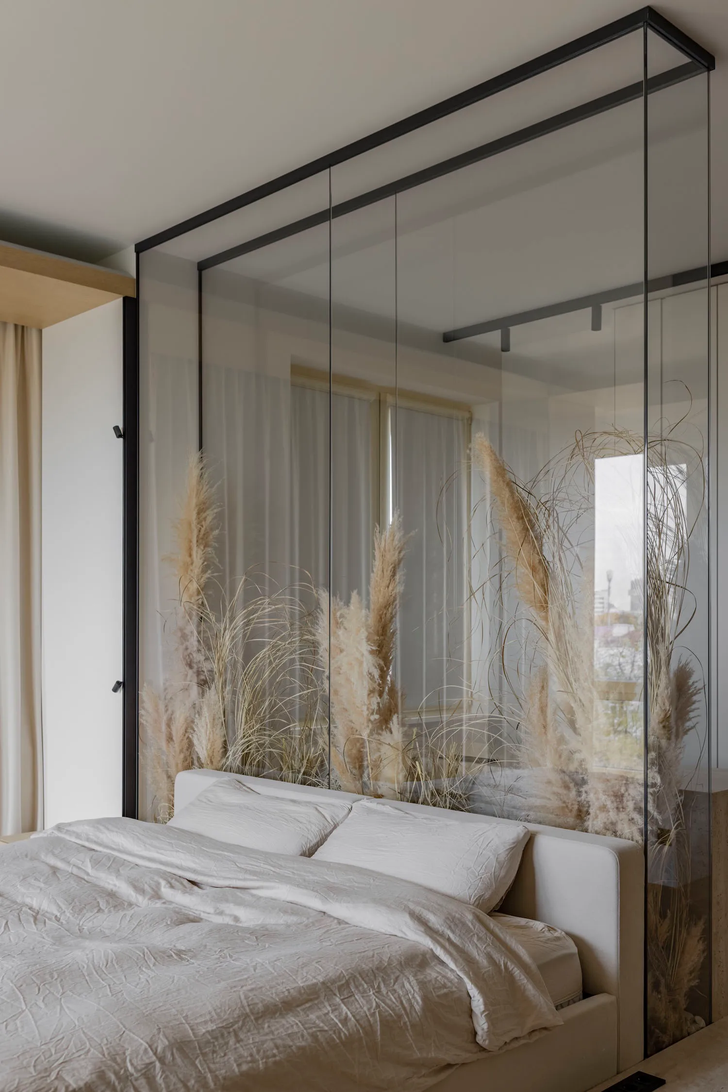 Bedroom featuring a bed with white bedding and pampas grass, behind a glass partition.