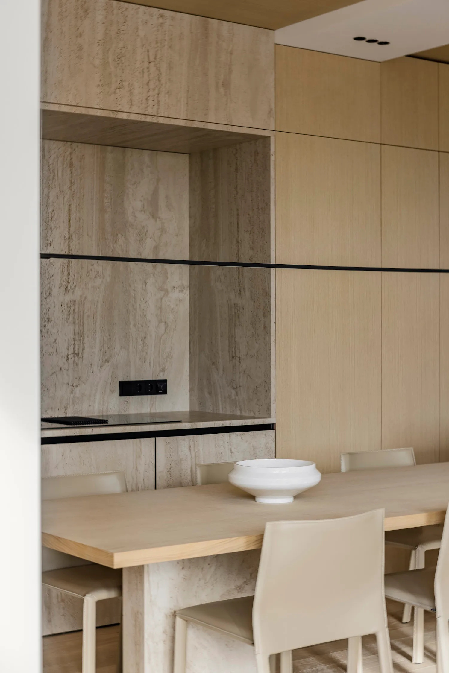 Modern dining room featuring a long table, chairs, and minimalist decor made of concrete and wood materials.
