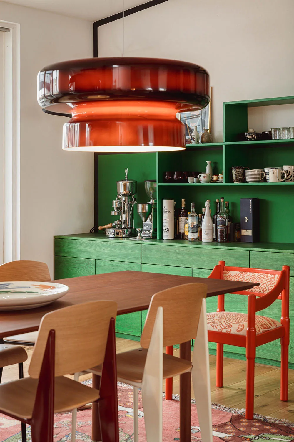 Modern interior design featuring wooden dining table, green shelves, and red chairs
