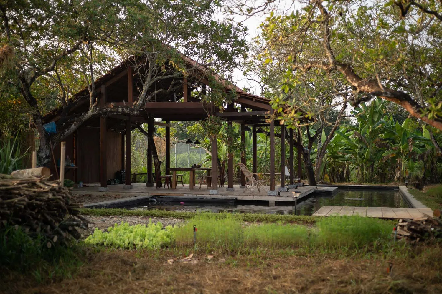 A wooden outdoor living structure with a pool and seating area surrounded by lush greenery.