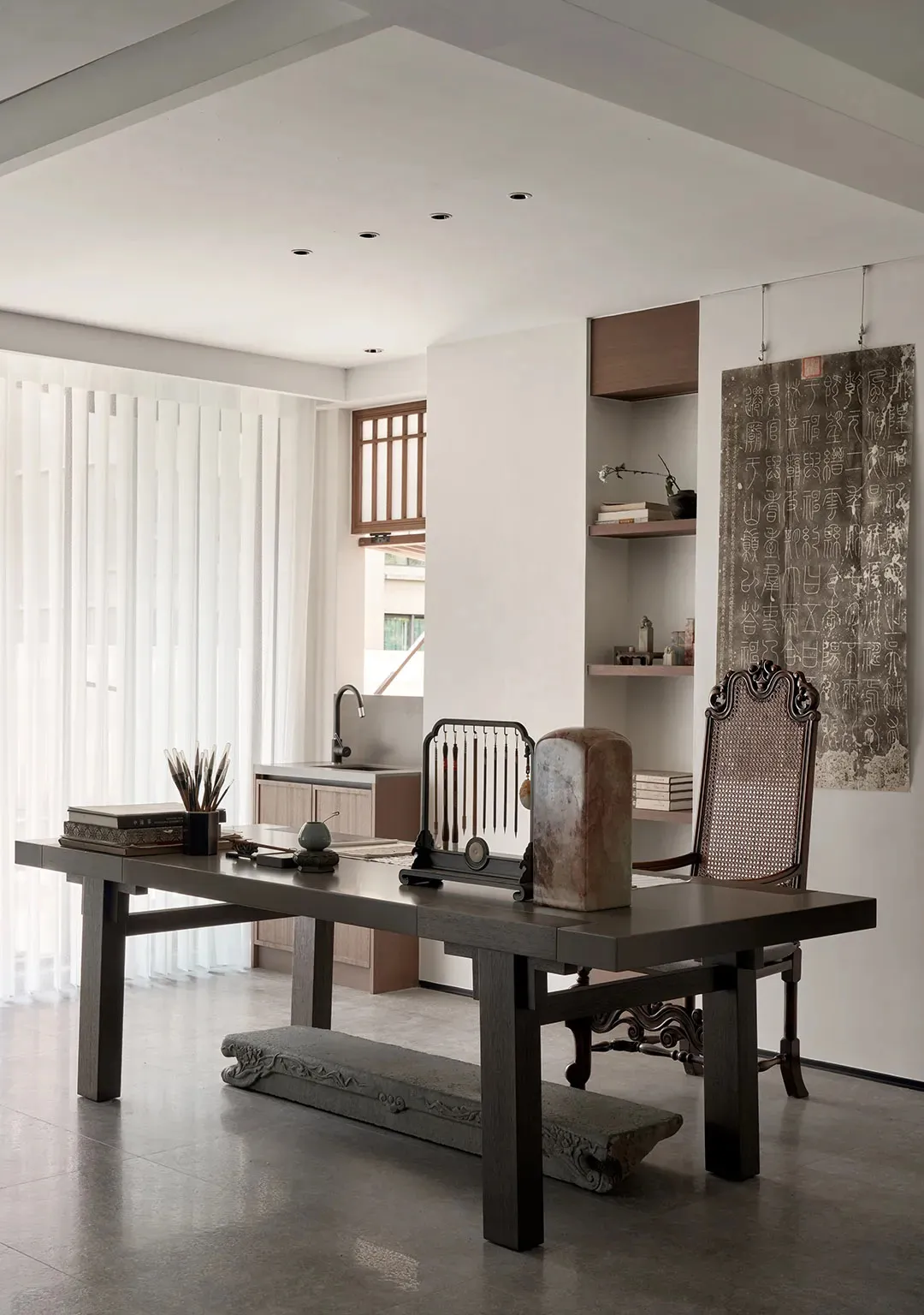 An office workspace featuring a traditional wooden table, pen holder, and a hanging scroll with Chinese calligraphy.