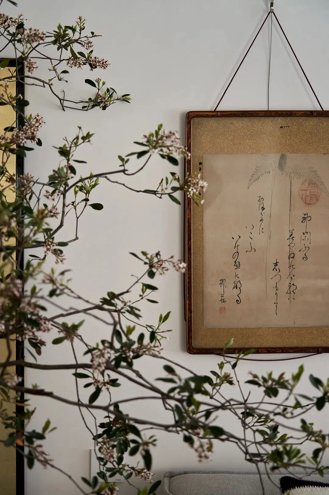 掛在白色牆面上的裝飾畫框,內有中式書法與植物插畫。