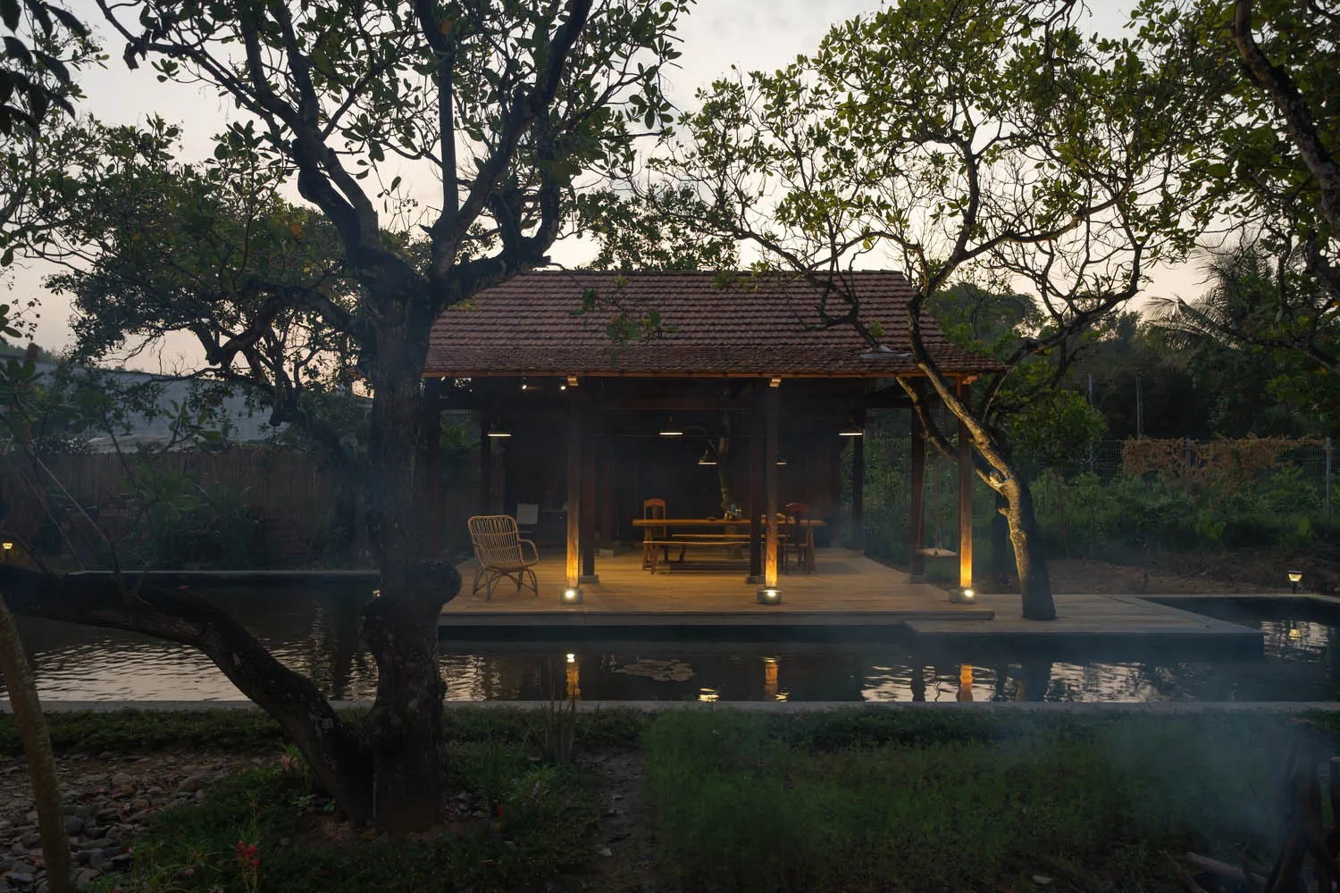 A minimalist outdoor living space featuring wood structures and a water feature surrounded by natural elements.