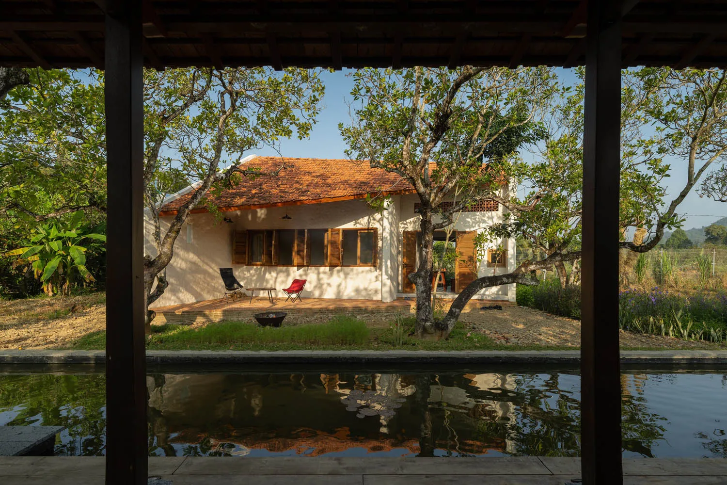 A minimalist residential home constructed of sandstone, surrounded by lush greenery and a tranquil pool.