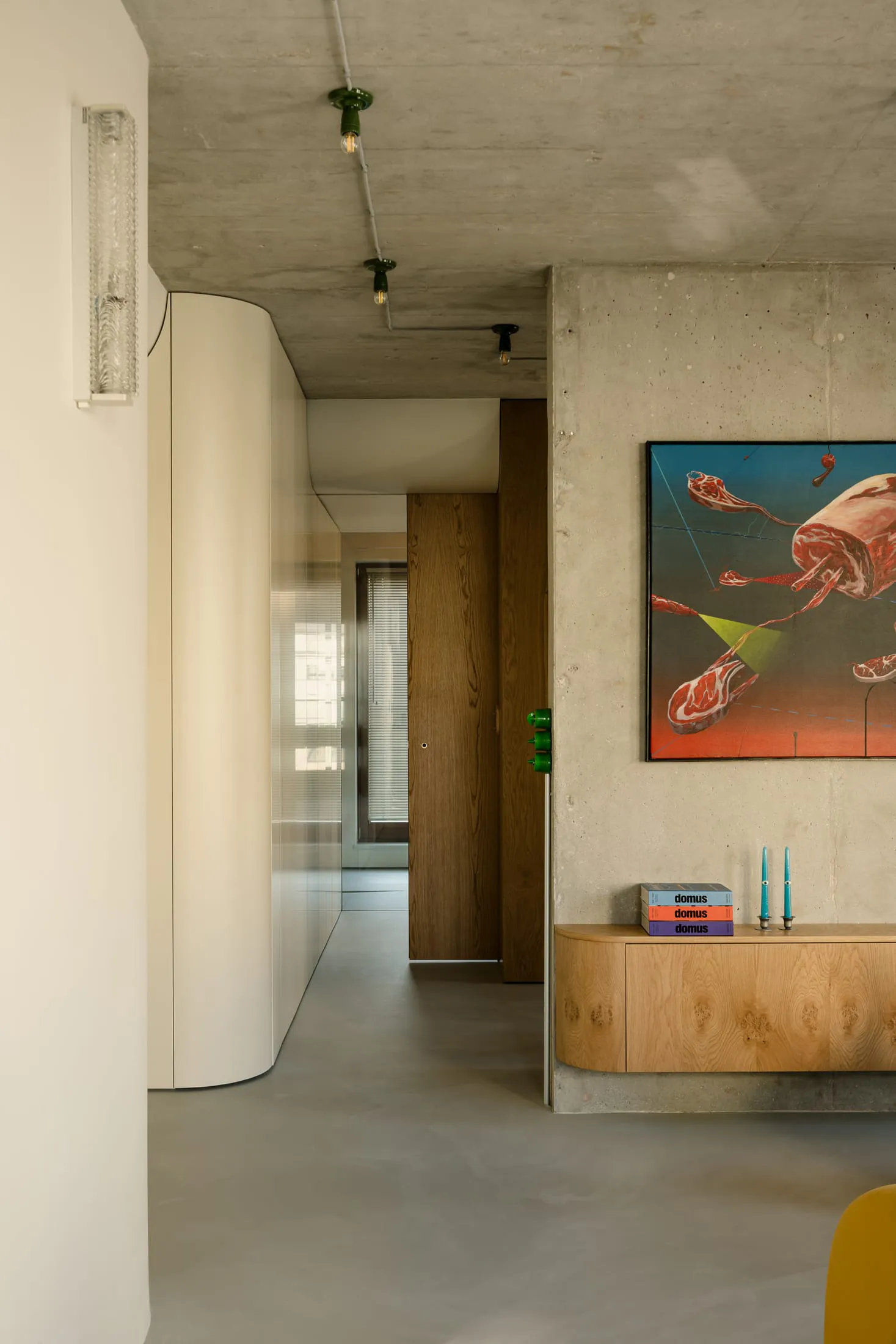 A modern entryway featuring concrete walls, a wooden cabinet, and a colorful abstract painting.