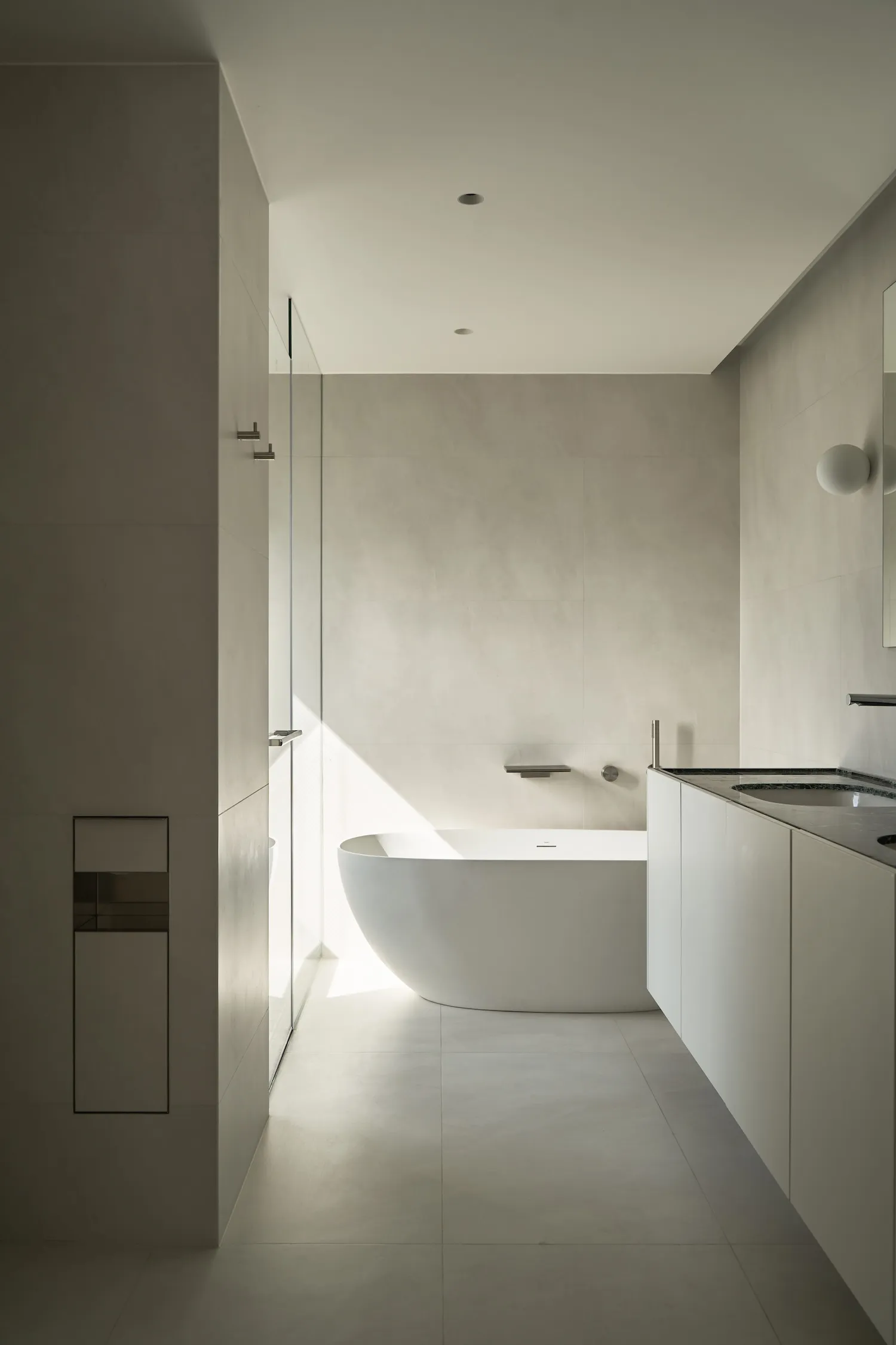 A minimalist bathroom with an open concept design, featuring a modern bathtub, a wall-mounted sink, and a glass shower door.