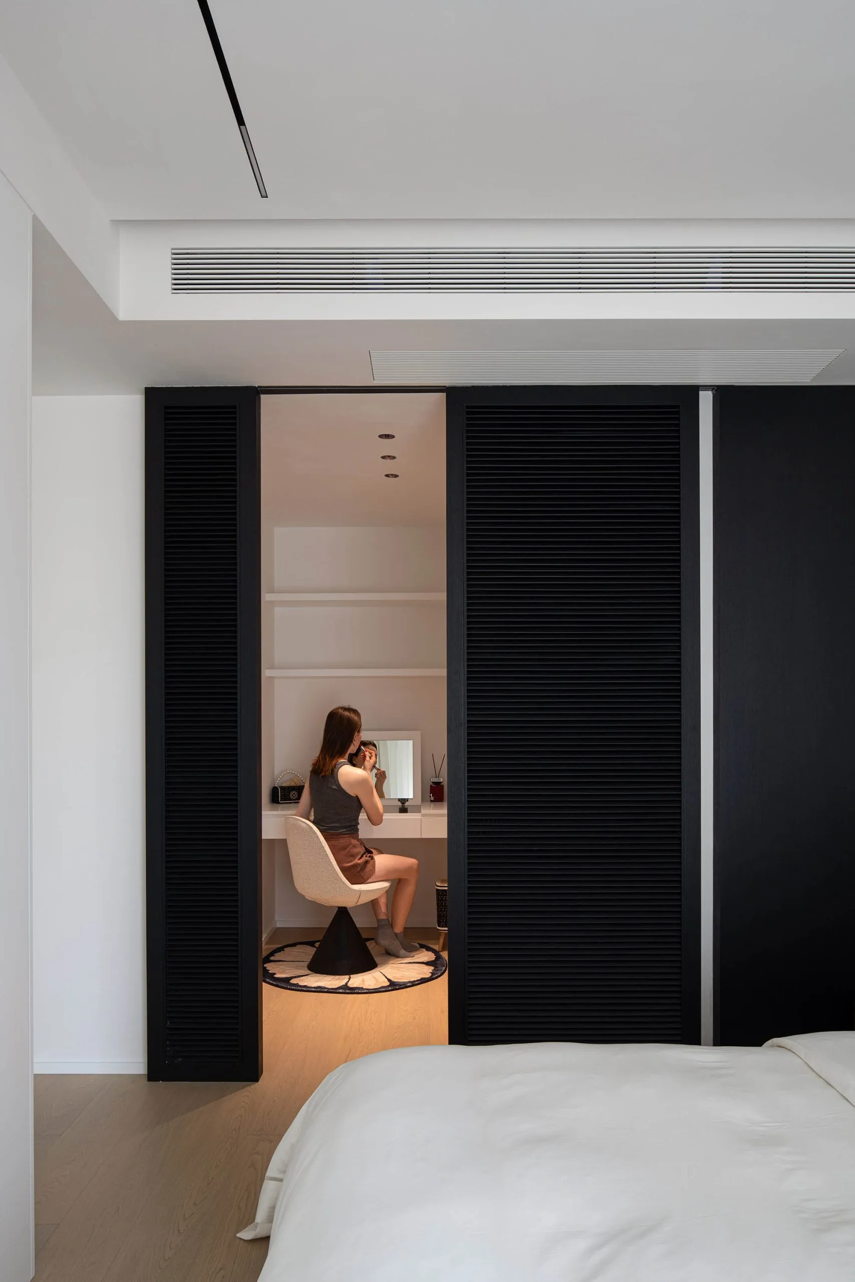 A minimalist bedroom with a white bed, black sliding shutters, and wooden flooring.