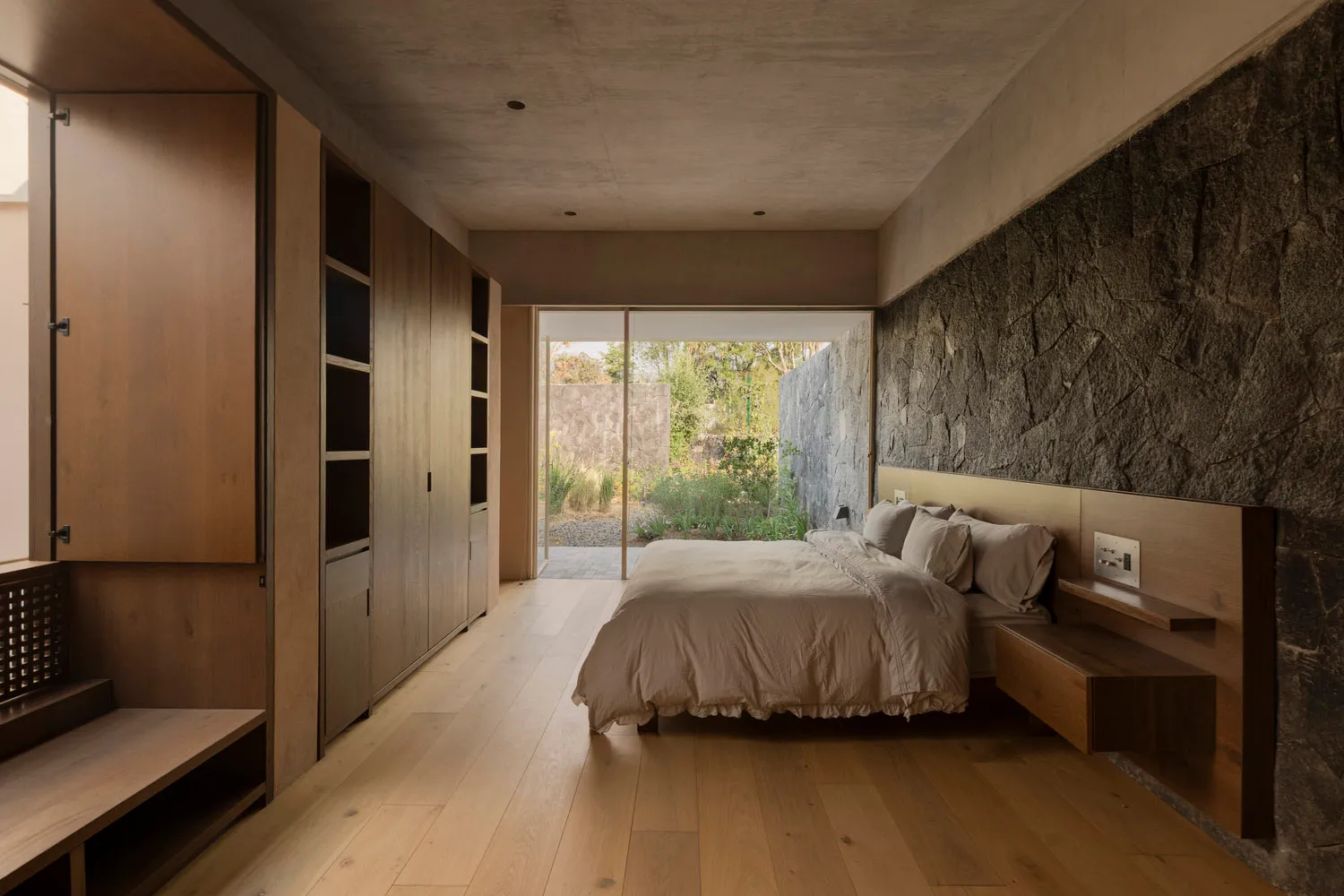 Minimalist bedroom featuring hardwood flooring and a stone wall.